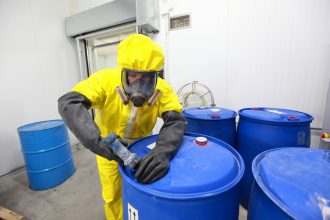 man in hazard suit opening large containers